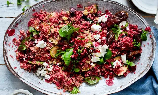 Rote Bete Bulgur Salat mit Granatapfelkernen, Feigen, Feta und frischen Kräutern auf einem ovalen Teller.