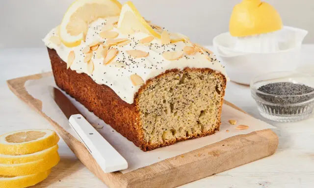 Saftiger zitronen mohn kuchen mit weißem Zuckerguss, Mandelsplittern und Mohn bestreut. Zitronenscheiben zieren die Oberseite.