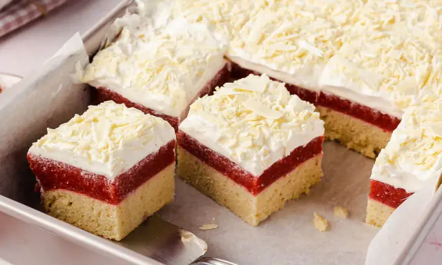 Schneeweiße Sahne und rote Fruchtschicht auf hellem Boden, bestreut mit weißer Schokolade. Ein köstlicher Frau Holle Kuchen, der zum Reinbeißen einlädt.