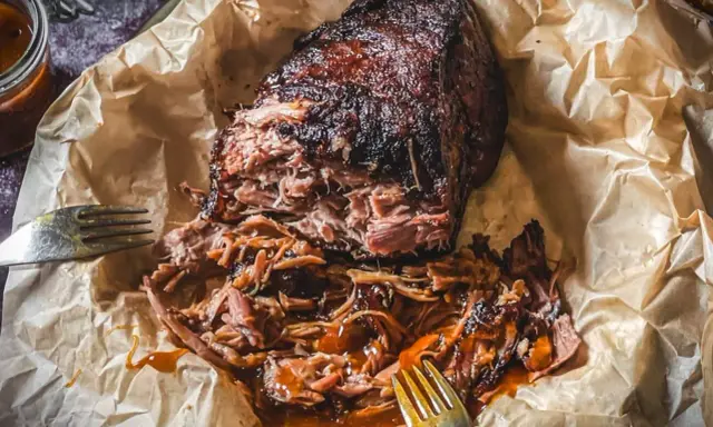 Saftiges pulled pork, zart zerfallen, mit BBQ-Sauce übergossen, auf Backpapier mit Gabeln.