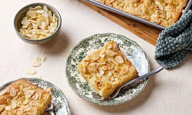 Ein Stück Butterkuchen mit Mandelblättchen auf einem Teller, daneben eine Schüssel mit Mandeln. Perfekt für ein Butterkuchen Rezept.