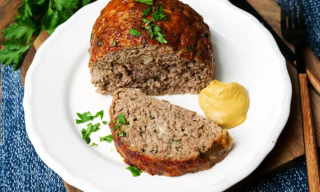 Saftiger hackbraten im ofen, auf einem Teller mit Senf und Petersilie garniert.