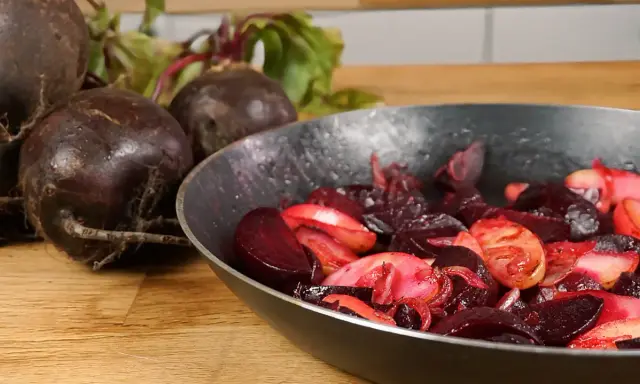 Rote Bete wird in einer Pfanne zubereitet, ein köstliches Hauptgericht. Frische Rote Bete liegt daneben.