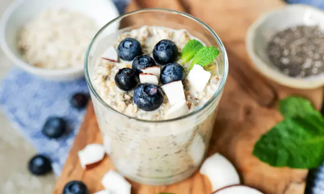 Ein Glas cremiger Overnight Oats mit Blaubeeren, Kokosnuss und Minze. Perfekt für ein schnelles Frühstück.
