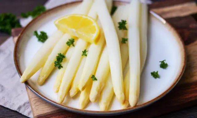 Frischer weißer Spargel, perfekt gekocht, garniert mit Petersilie und einer Zitronenspalte auf einem Teller. Ein Genuss, wenn Spargel Saison hat.