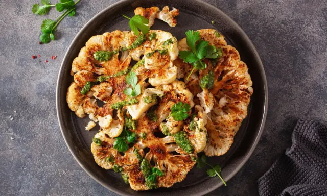 Geröstete blumenkohlscheiben im backofen, beträufelt mit grüner Soße und garniert mit Koriander.