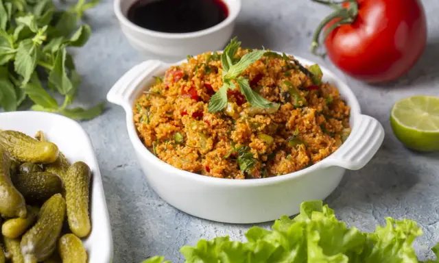 Ein köstliches Kisir-Rezept mit Bulgur, Tomaten und Kräutern, garniert mit Minze. Daneben Cornichons, Granatapfelsirup, Limette und ein frischer Kopfsalat.