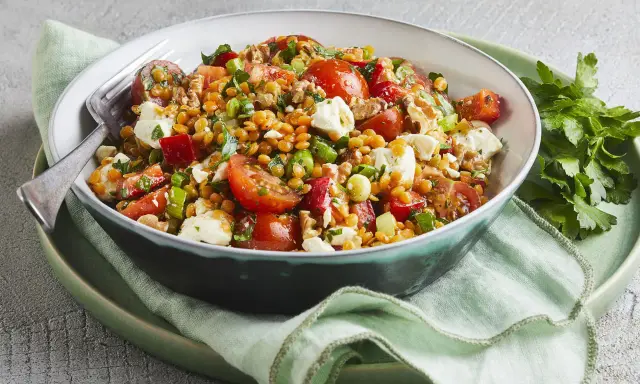 Ein bunter, gesunder rote Linsen Salat mit Tomaten, Feta und Nüssen, appetitlich in einer Schüssel serviert.