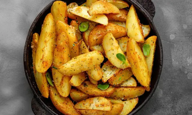 Goldbraune Ofenkartoffeln, gewürzt mit Kräutern, in einer schwarzen Pfanne. Perfekt für ein einfaches Ofenkartoffeln Rezept.