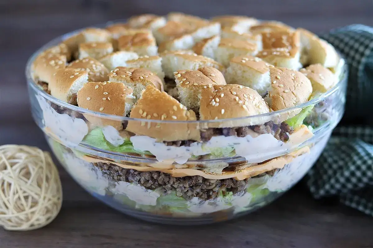 Schichtsalat im Glas, der wie ein Big Mac Salat aussieht, mit Hackfleisch, Salat, K&auml;se und Br&ouml;tchenst&uuml;cken.