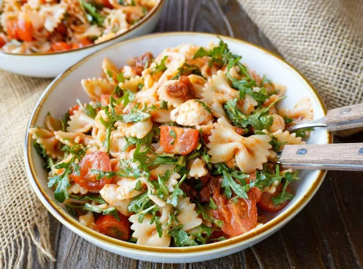 Ein k&ouml;stlicher italienischer Nudelsalat mit Farfalle, Kirschtomaten, Mozzarella und Rucola, serviert in einer Sch&uuml;ssel.