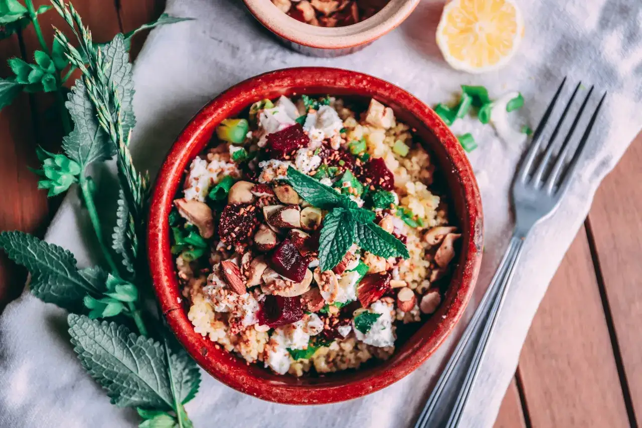 Rote Bete Bulgur Salat mit N&uuml;ssen und Kr&auml;utern in einer roten Schale, garniert mit Minze.