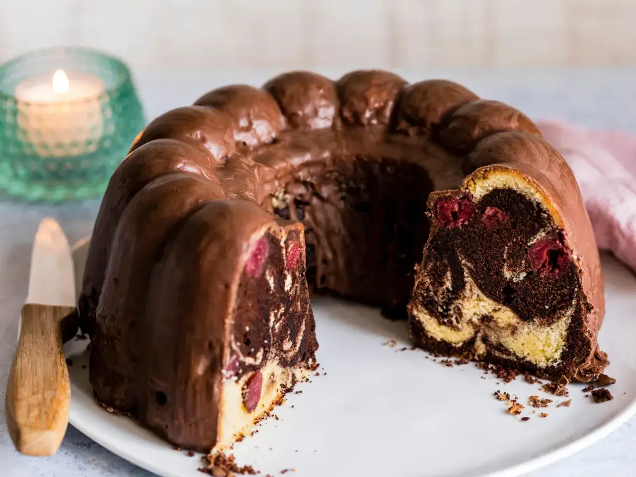 Ein saftiger Marmorkuchen mit Kirschen, &uuml;berzogen mit Schokolade. Ein St&uuml;ck ist angeschnitten und zeigt die leckere Maserung.