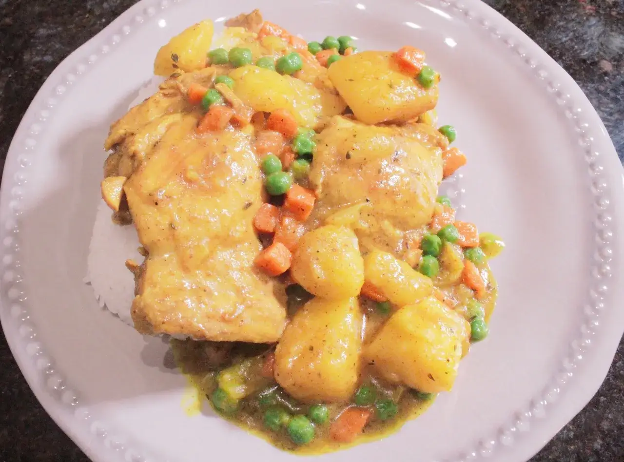 Colombo de poulet mit Kartoffeln, Erbsen und Karotten in einer cremigen Sauce auf Reis serviert.