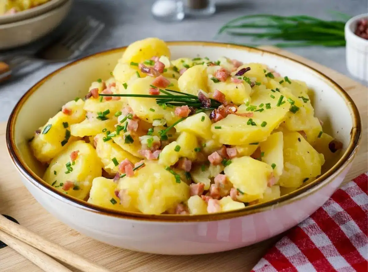 Ein Teller mit warmem Kartoffelsalat, garniert mit Speckw&uuml;rfeln und Schnittlauch.