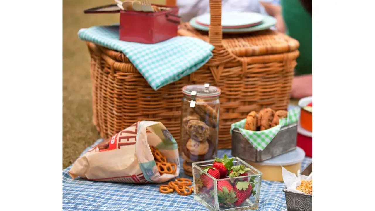 Picknick-Korb mit Brezeln, Keksen, Erdbeeren und anderen leckeren Picknick-Snacks auf einer karierten Decke.