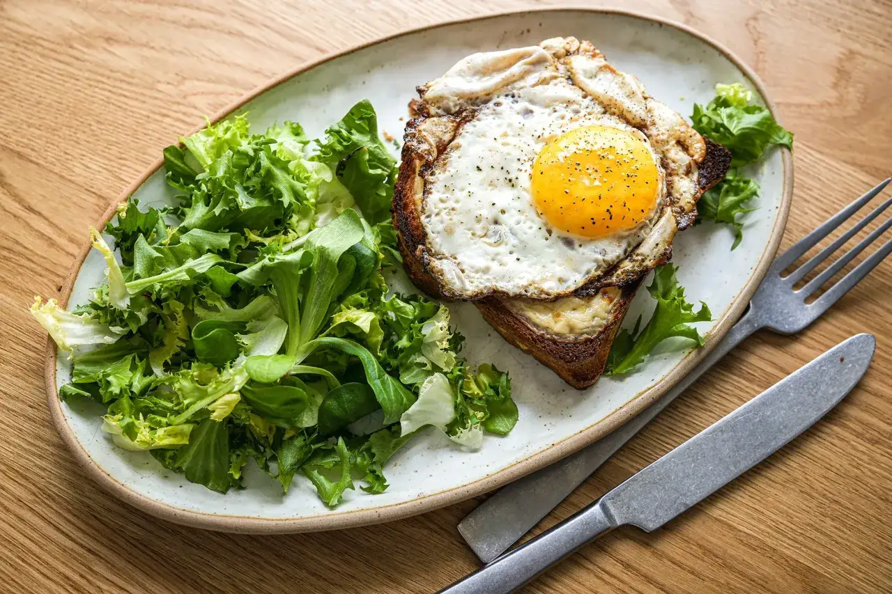 Ein Croque Madame mit Spiegelei, K&auml;se und Toast, serviert mit einem frischen Salat.