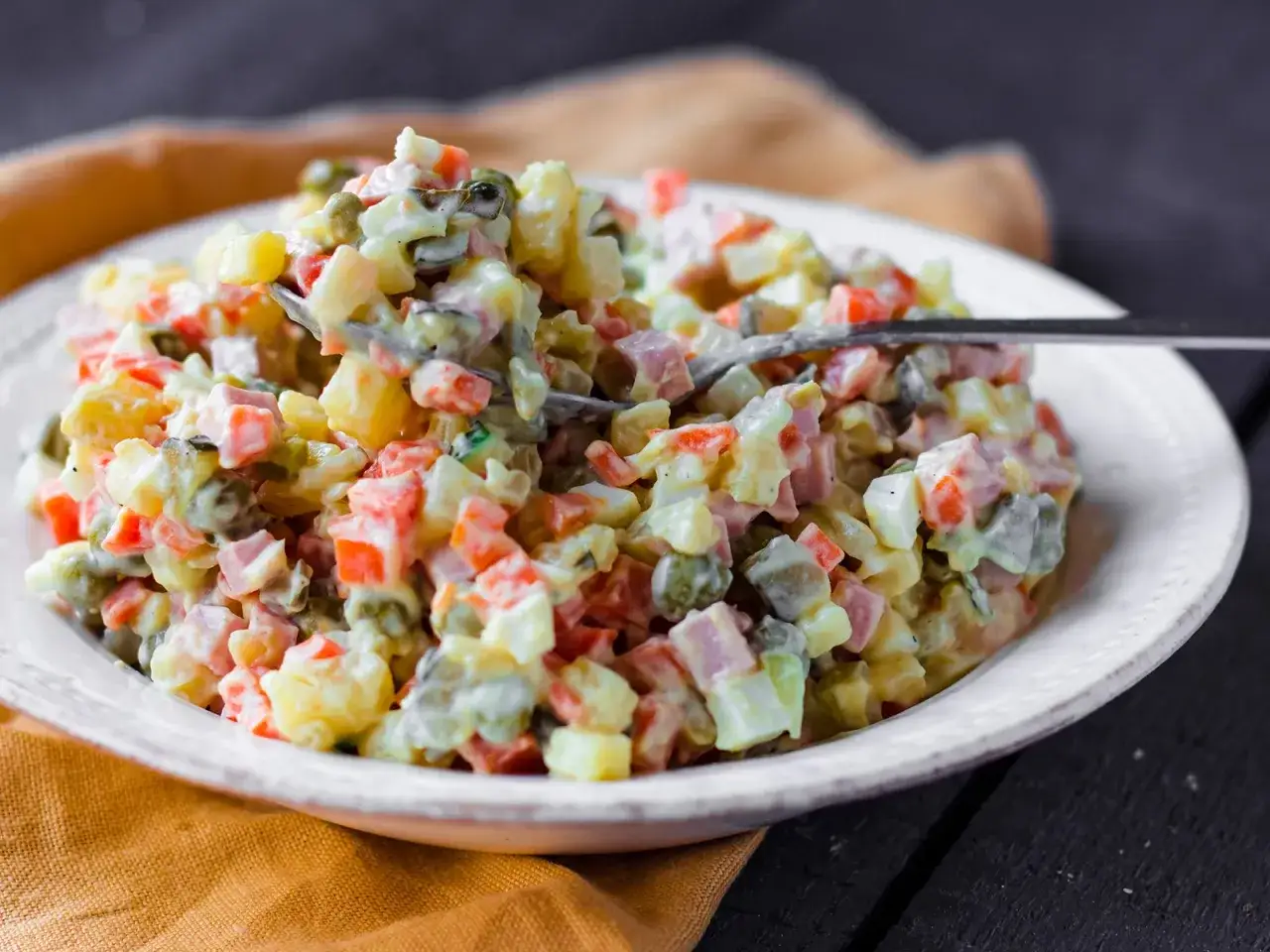 Ein L&ouml;ffel voller Olivier Salat, mit Kartoffeln, Erbsen, Karotten und Schinken in cremiger Mayonnaise.