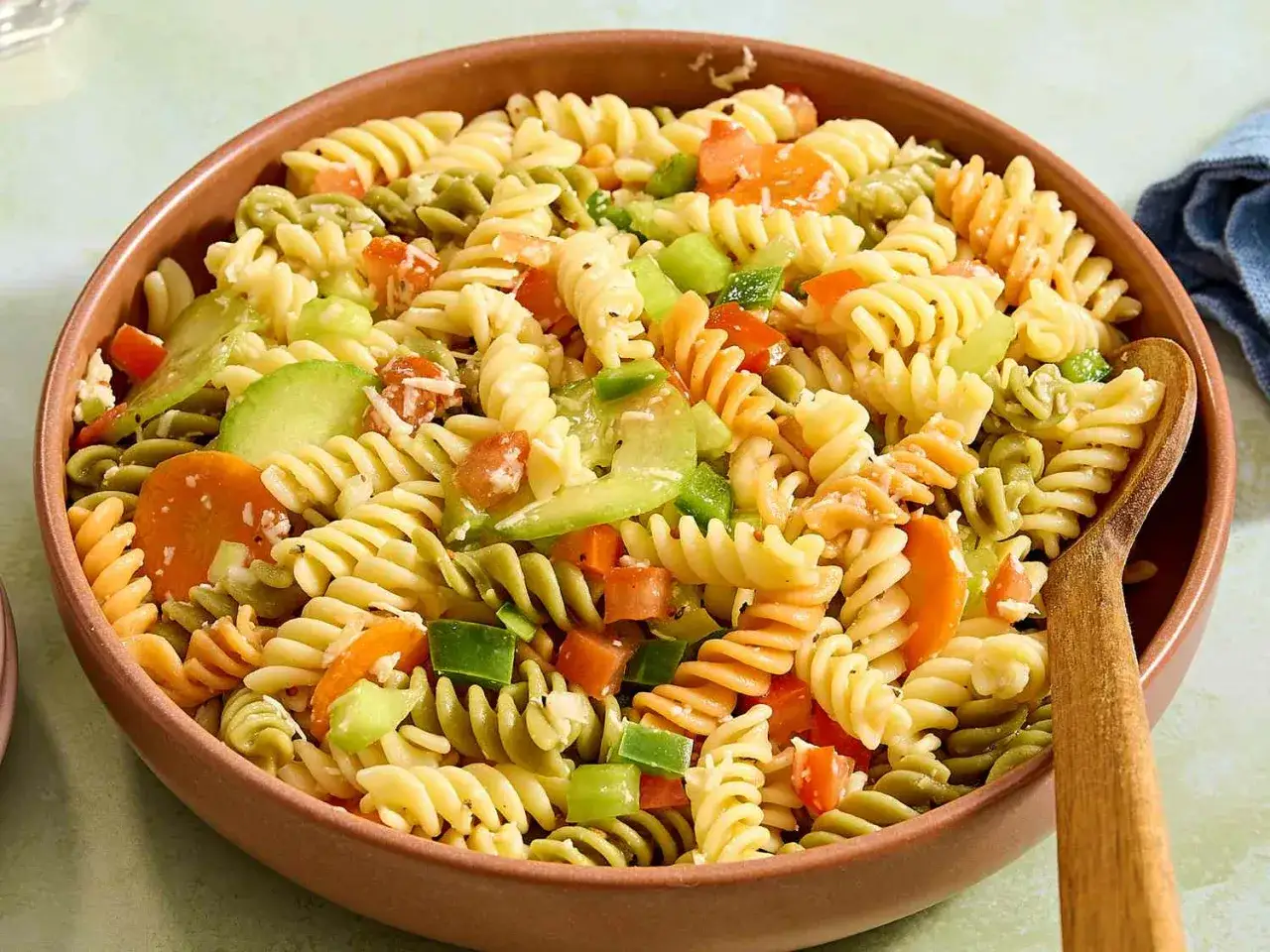 Bunter Nudelsalat ohne Mayo mit Spiralnudeln, Karotten, Paprika und Gurke in einer braunen Sch&uuml;ssel.