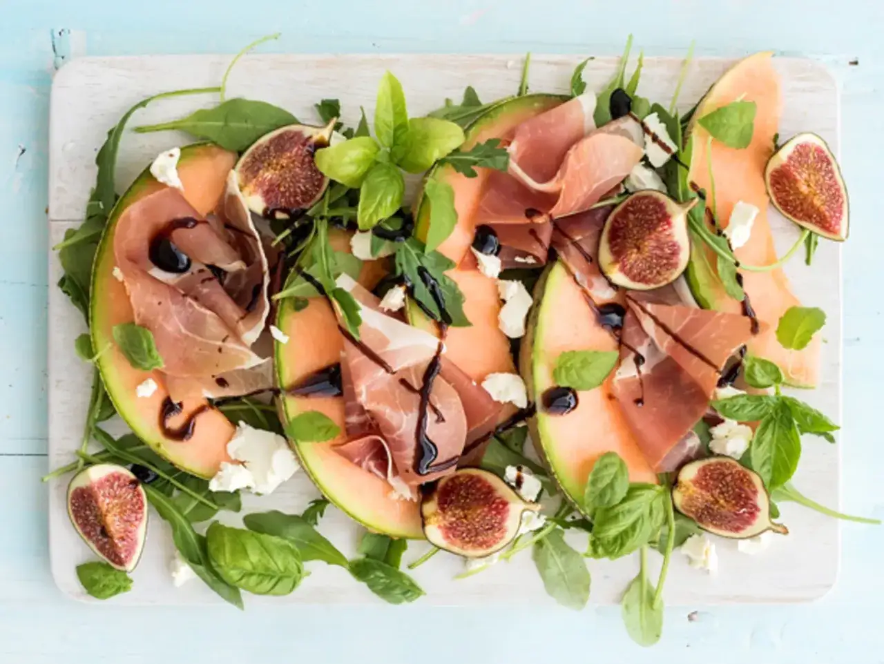 Melone mit Schinken, Feigen, Rucola und Balsamico-Dressing auf einem Brett. Ein leichter Sommergenuss.