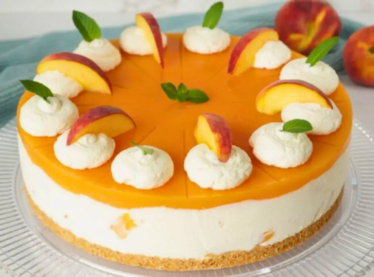 Pfirsichtorte mit Biskuitboden, cremiger F&uuml;llung und Pfirsichgelee. Dekoriert mit Pfirsichspalten, Klecksen und Minze. Eine k&ouml;stliche torte ohne sahne.