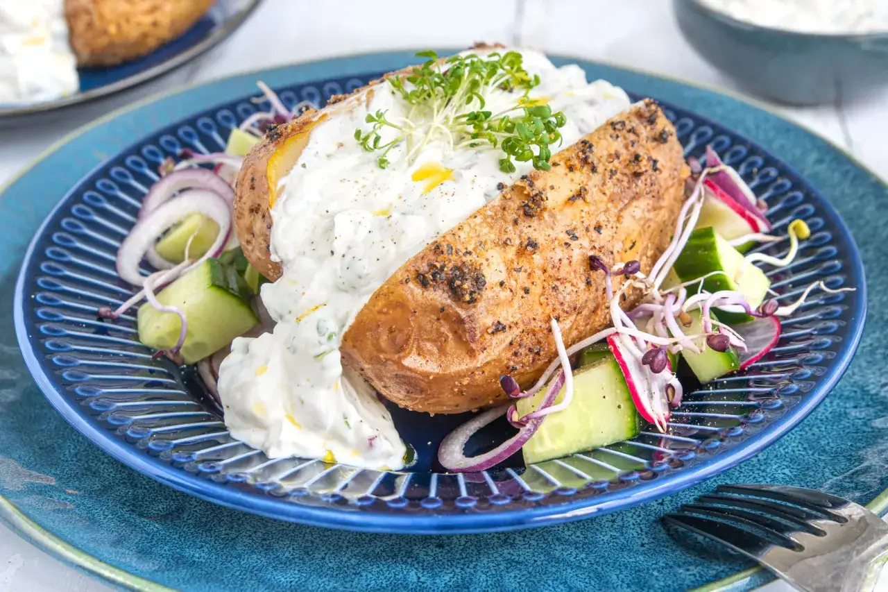 Ofenkartoffeln rezept: Eine gebackene Kartoffel mit Kr&auml;uterquark, Gurken, Radieschen und roten Zwiebeln auf einem blauen Teller.