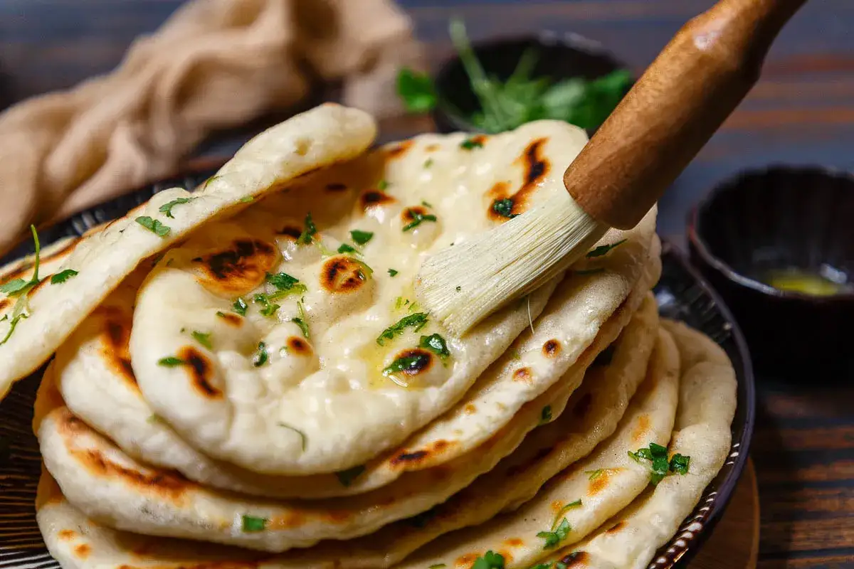 Frisch gebackenes Naan Brot wird mit Butter bestrichen und mit Kr&auml;utern bestreut.