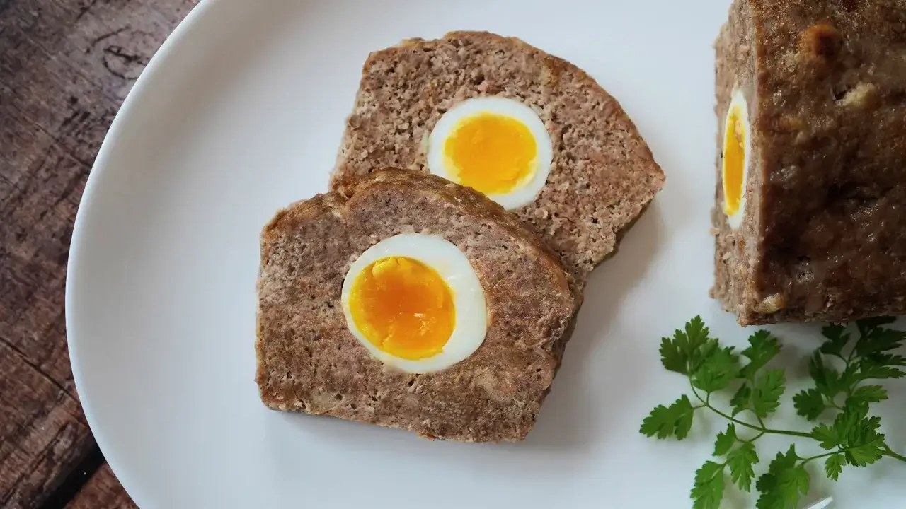 Zwei Scheiben Hackbraten im Ofen mit gekochtem Ei im Inneren, garniert mit Petersilie.