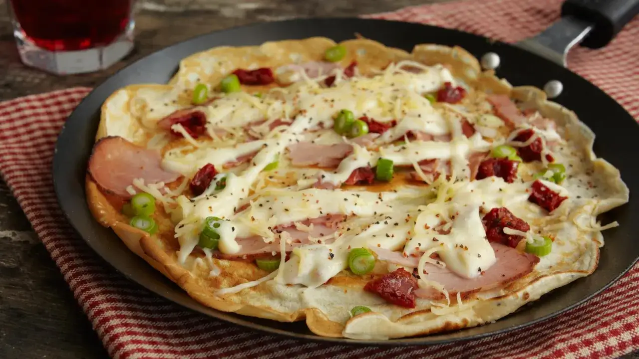 Herzhafte Pfannkuchen mit Schinken, K&auml;se, getrockneten Tomaten und Fr&uuml;hlingszwiebeln, &uuml;berbacken und in der Pfanne serviert.