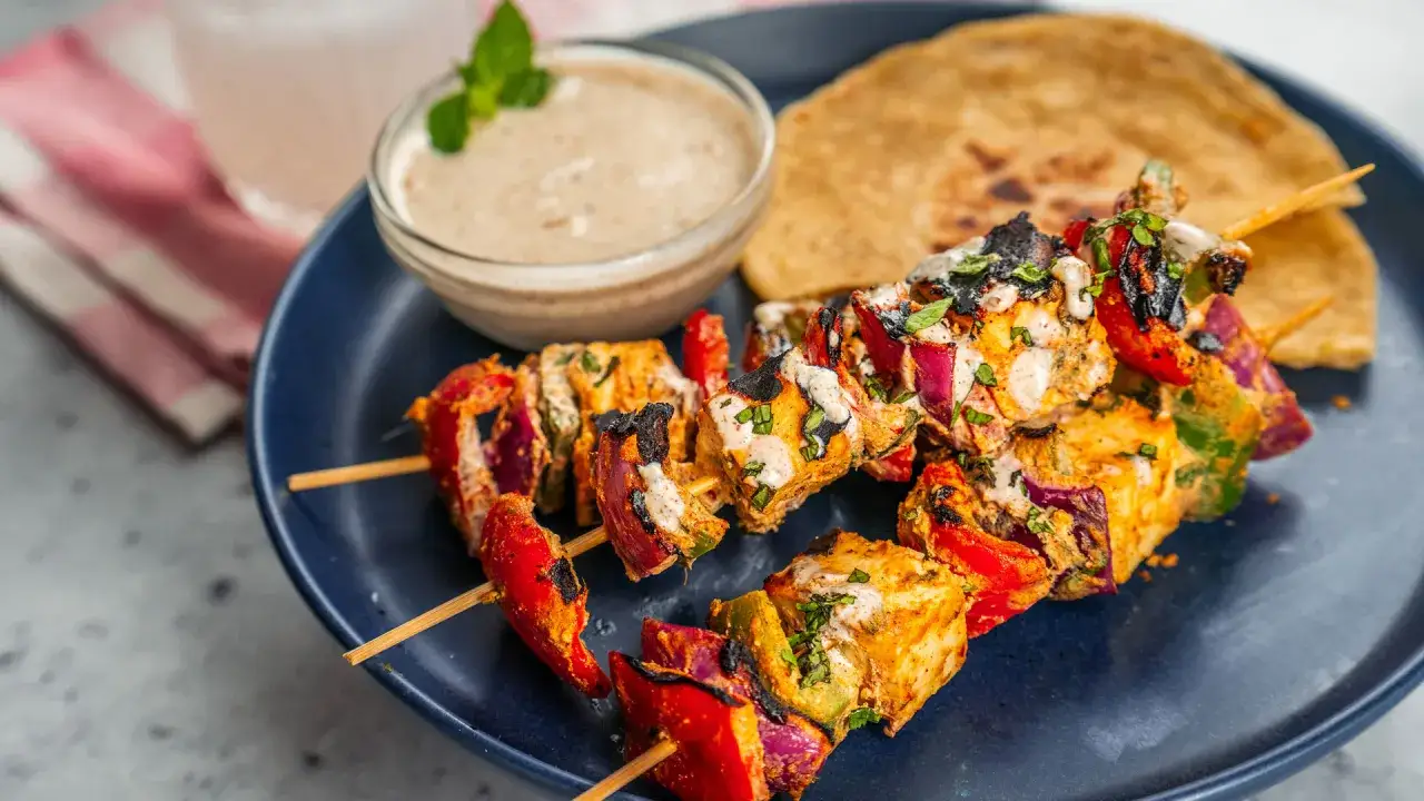 Saftige paneer tikka Spie&szlig;e mit Paprika und Zwiebeln, garniert mit Kr&auml;utern und Sauce, serviert mit Fladenbrot.