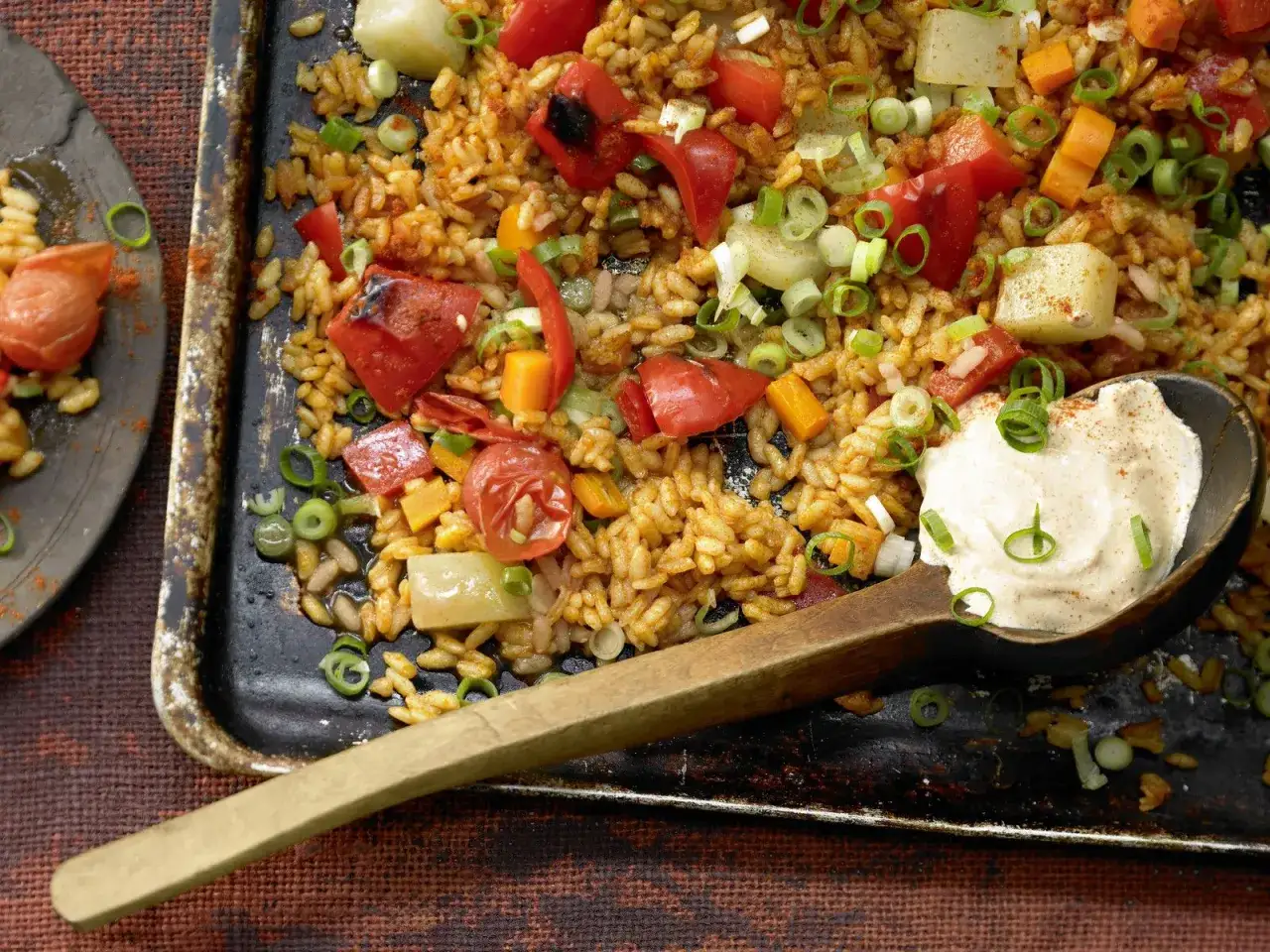 Leckerer One Pot Reis aus dem Ofen mit Paprika, Tomaten und Fr&uuml;hlingszwiebeln, serviert mit einer cremigen Sauce.