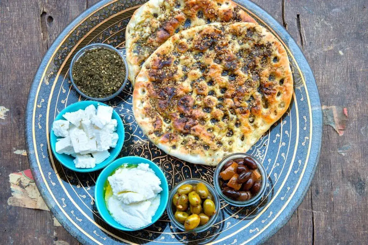 Fladenbrot mit Zatar, K&auml;se, Oliven und cremiger Paste auf einem verzierten Tablett. Was ist Zatar? Eine w&uuml;rzige Mischung aus Kr&auml;utern, Sesam und Gew&uuml;rzen.