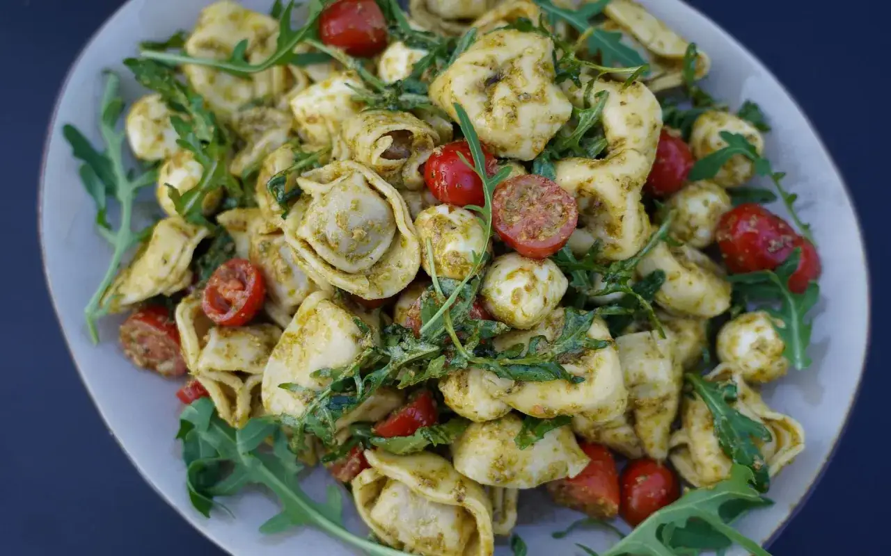 Ein k&ouml;stlicher tortellinisalat mit pesto, garniert mit Kirschtomaten, Mozzarella-Kugeln und Rucola.