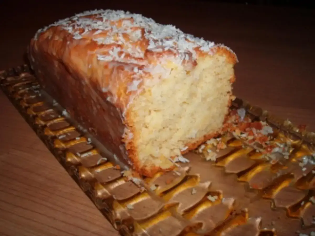 Ein saftiger Ananas Kokos Kuchen, mit Zuckerguss und Kokosraspeln bestreut, auf einem goldenen Tablett.