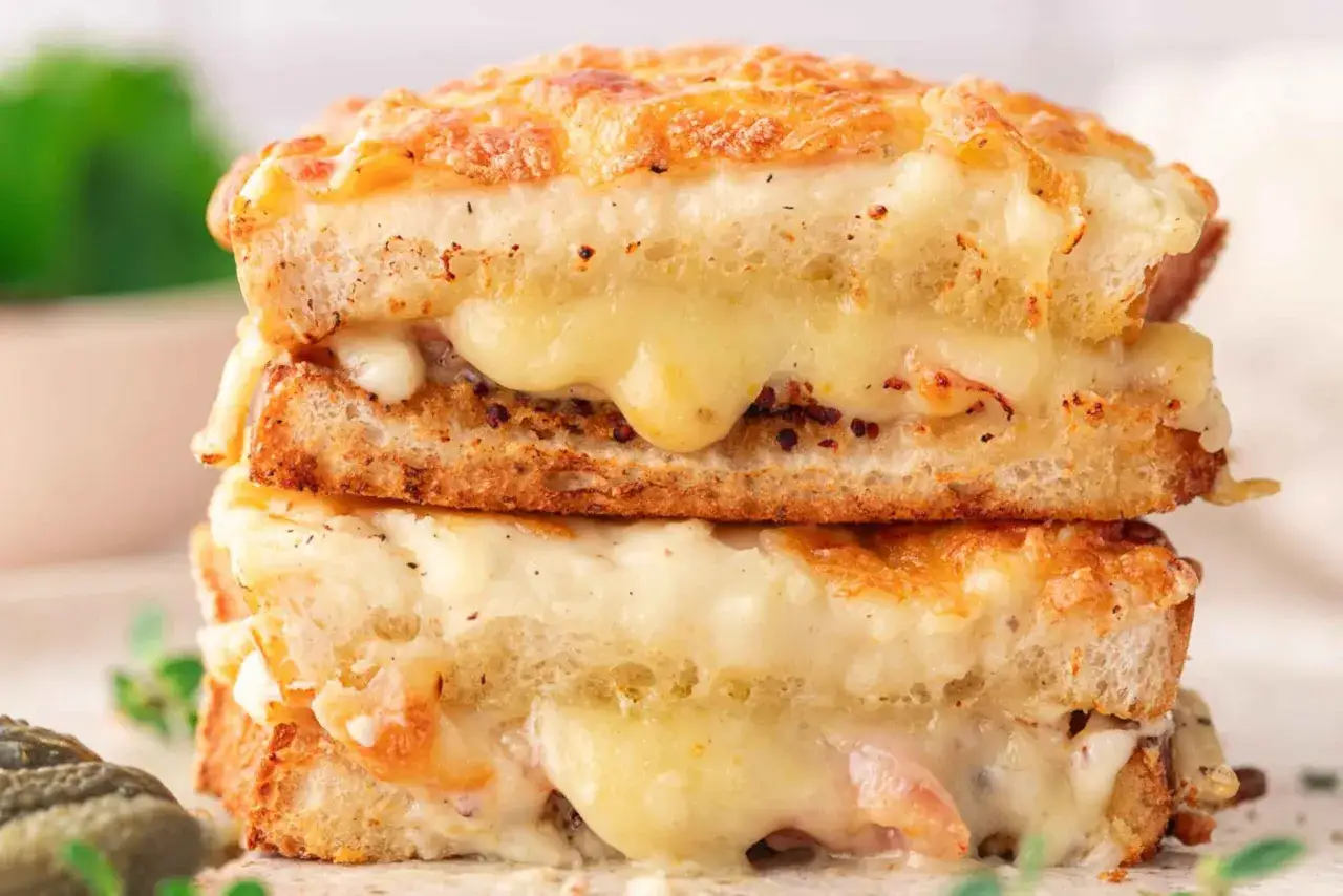 Zwei gestapelte, goldbraun gebackene Croque Monsieur mit geschmolzenem K&auml;se, der herausl&auml;uft.