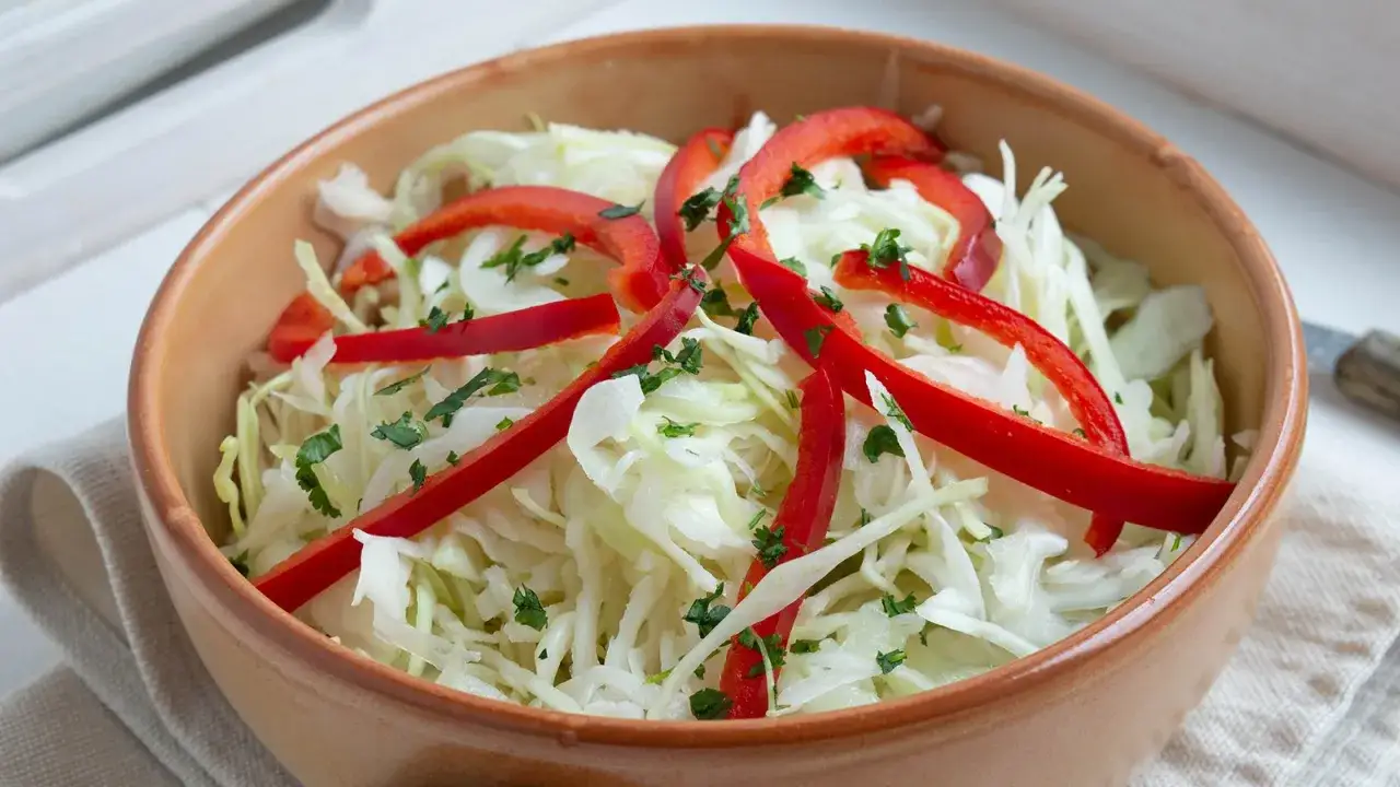 Frischer Krautsalat selbst machen: Fein gehobelter Wei&szlig;kohl mit roten Paprikastreifen und Petersilie in einer Sch&uuml;ssel.