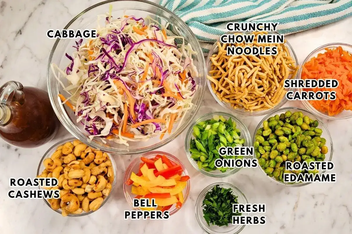 Zutaten f&uuml;r einen Asia Salat: Kohl, Karotten, Edamame, Cashews, Paprika, Fr&uuml;hlingszwiebeln, Kr&auml;uter, Nudeln und Dressing.