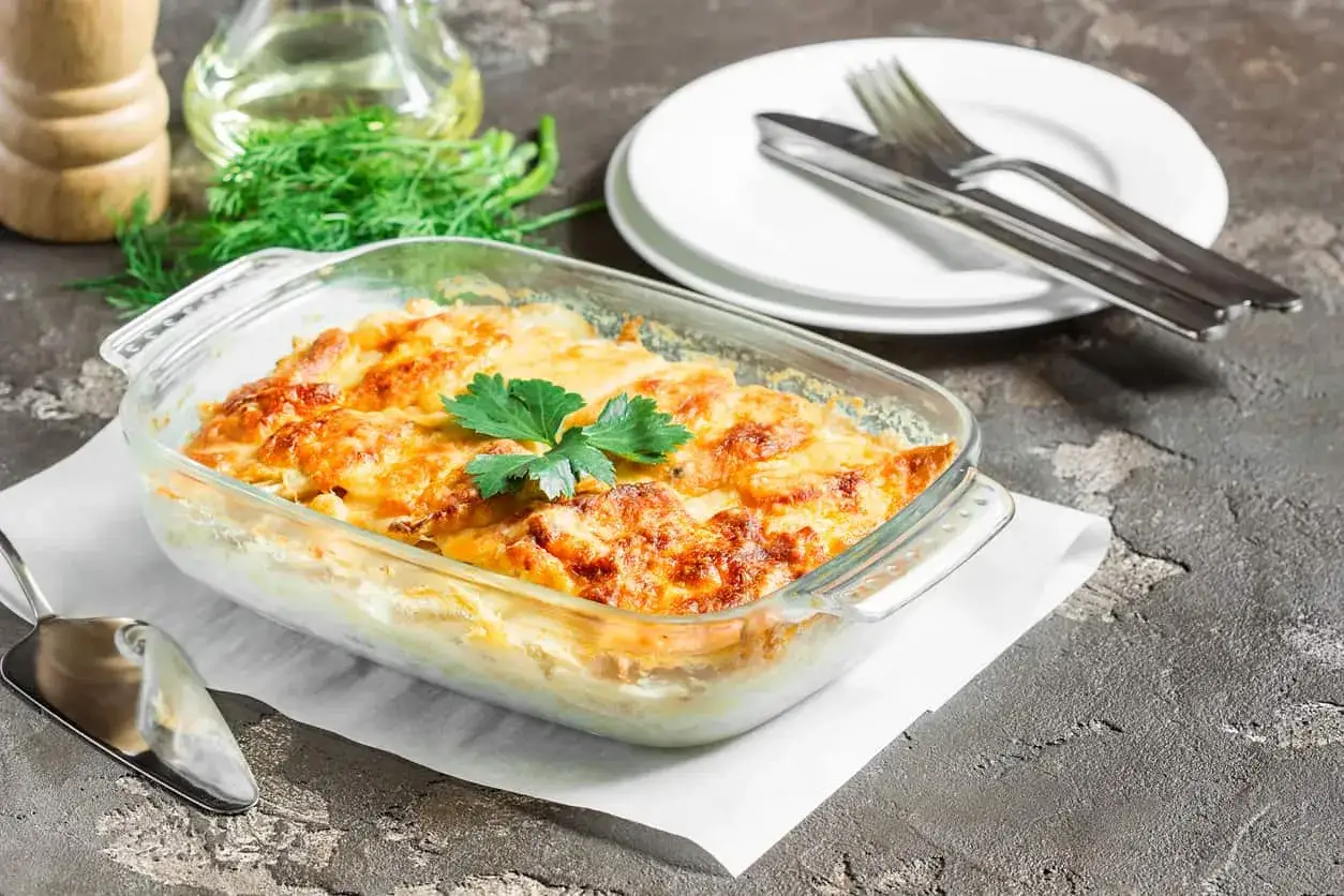 Goldbrauner Kohlrabi-Auflauf vegetarisch in Auflaufform, garniert mit Petersilie. Daneben Teller und Besteck.
