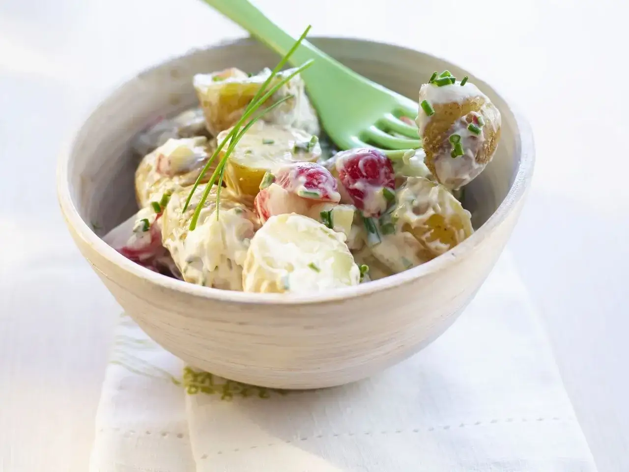 Ein cremiger Kartoffelsalat mit Joghurt, Radieschen und Schnittlauch in einer Holzschale, garniert mit frischen Kr&auml;utern.