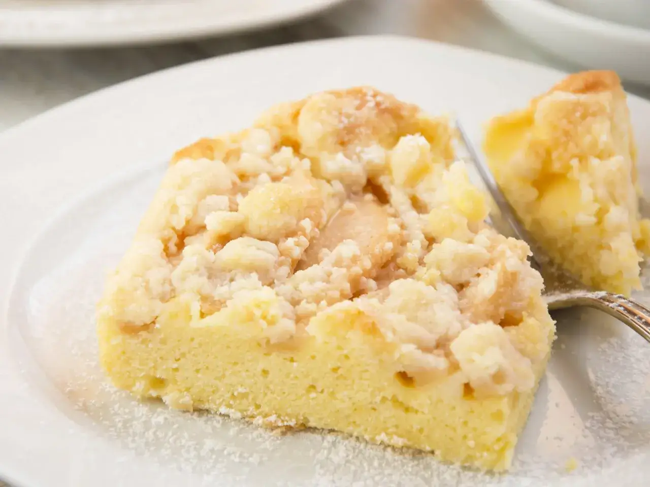 Ein St&uuml;ck saftiger Kuchen mit Apfelmus und Streuseln, best&auml;ubt mit Puderzucker.