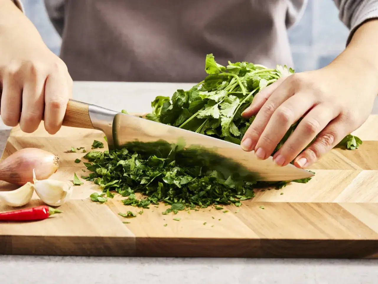 Frische Kr&auml;uter werden gehackt. Wer den Koriander Geschmack neutralisieren m&ouml;chte, kann ihn mit anderen Kr&auml;utern mischen. Zwiebel, Knoblauch und Chili liegen bereit.