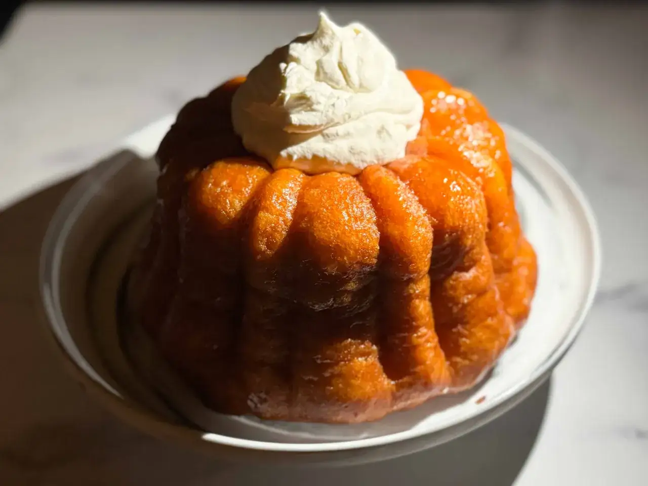 Ein glänzender Baba au Rhum, getoppt mit einer Sahnehaube, auf einem Teller.