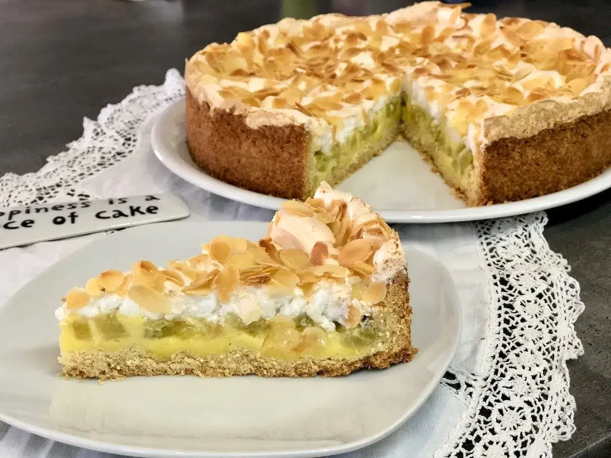 Ein k&ouml;stlicher Rhabarberkuchen mit Pudding und Baiser, bestreut mit Mandelbl&auml;ttchen. Ein St&uuml;ck Gl&uuml;ck auf einem Teller.