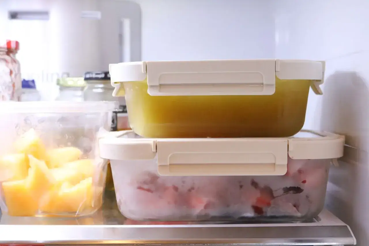 Vorratsbeh&auml;lter mit gelber Fl&uuml;ssigkeit und gefrorenen Beeren im K&uuml;hlschrank, bereit f&uuml;r Meal Prep zum Einfrieren.