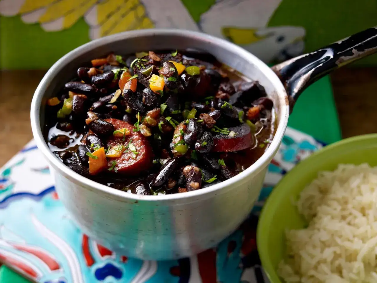Herzhaftes schwarze bohnen rezept im Topf, mit Wurst und Gem&uuml;se, daneben eine Sch&uuml;ssel Reis.