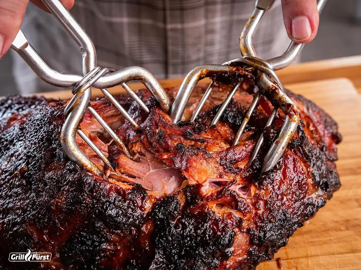 Zwei Fleischgabeln zerrei&szlig;en ein saftiges, langsam gegartes pulled pork mit dunkler Kruste.