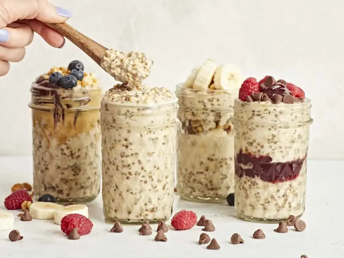 Vier Gl&auml;ser mit Overnight Oats Grundrezept, garniert mit Beeren, Bananen und Schokost&uuml;ckchen.