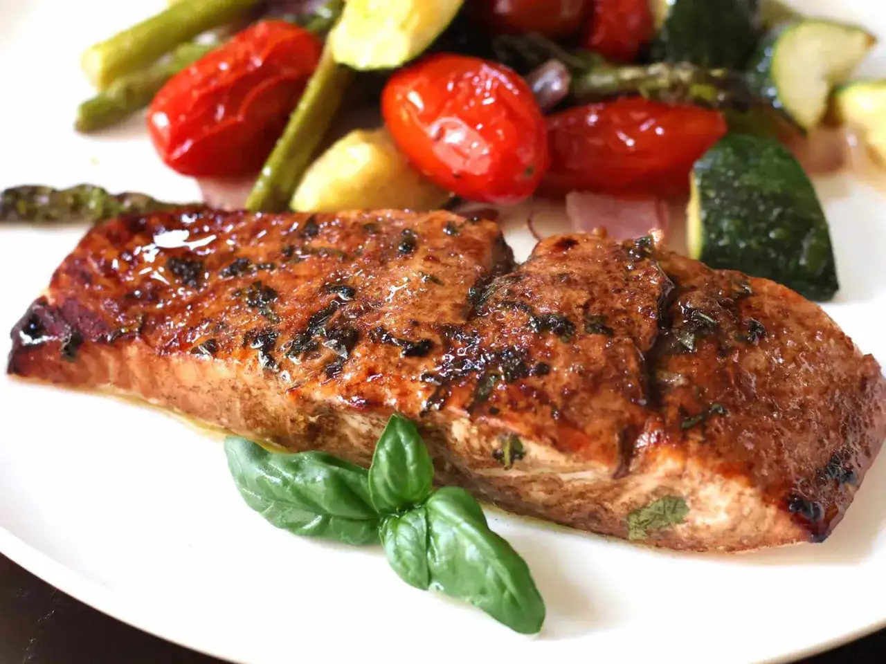 Saftiger Lachs mediterran ofen, mit gebratenem Gem&uuml;se wie Tomaten, Zucchini und Spargel, garniert mit frischem Basilikum.