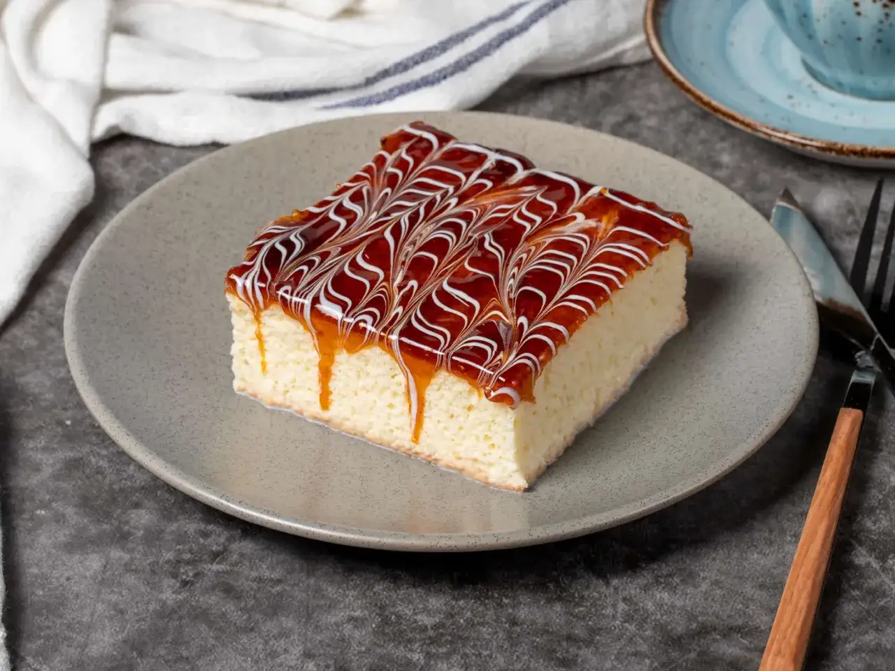 Ein St&uuml;ck saftiger Tres Leches Kuchen mit Karamell und wei&szlig;er Glasur, serviert auf einem grauen Teller.