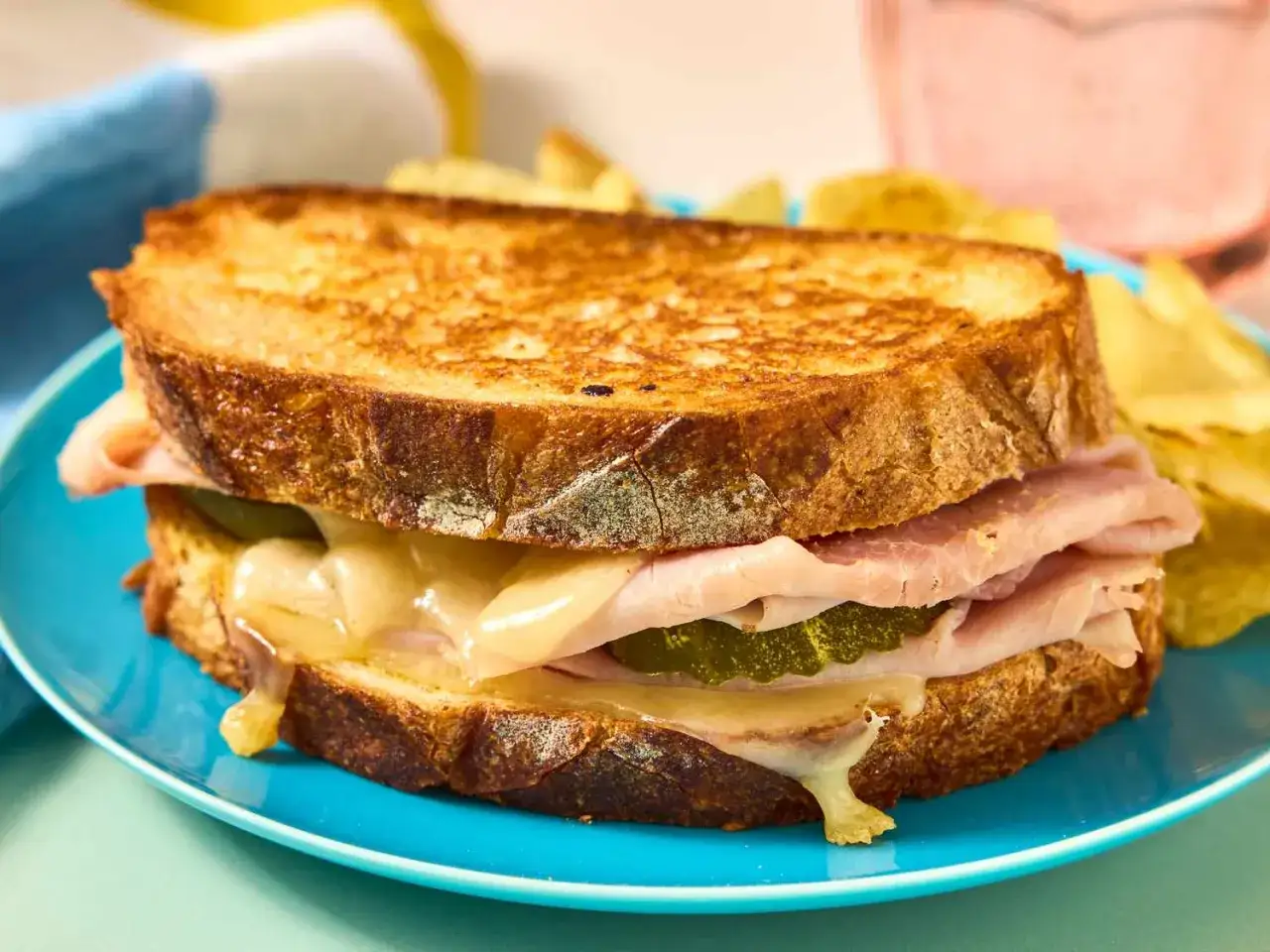 Ein goldbraunes Sandwich im Airfryer, gef&uuml;llt mit Schinken, K&auml;se und Gurken, serviert mit Kartoffelchips.